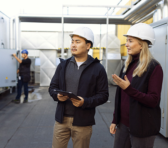 To mennesker står på en byggeplads og taler sammen med hvide hjelme på