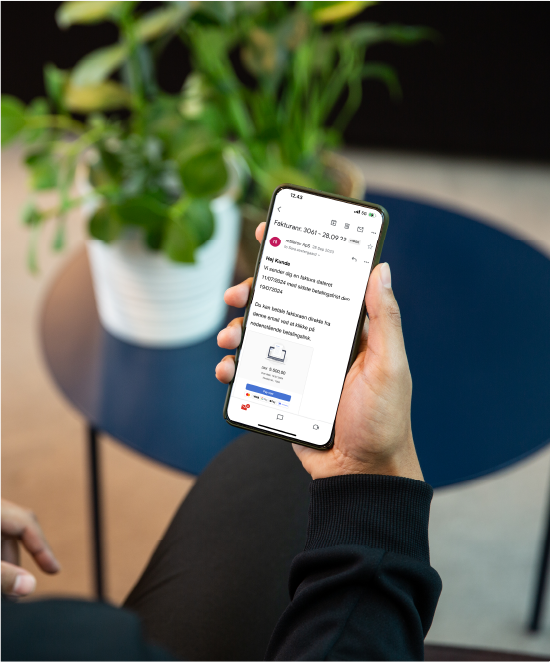 mand med telefon i hånd kigger på betalingslink mail ved bord med plante