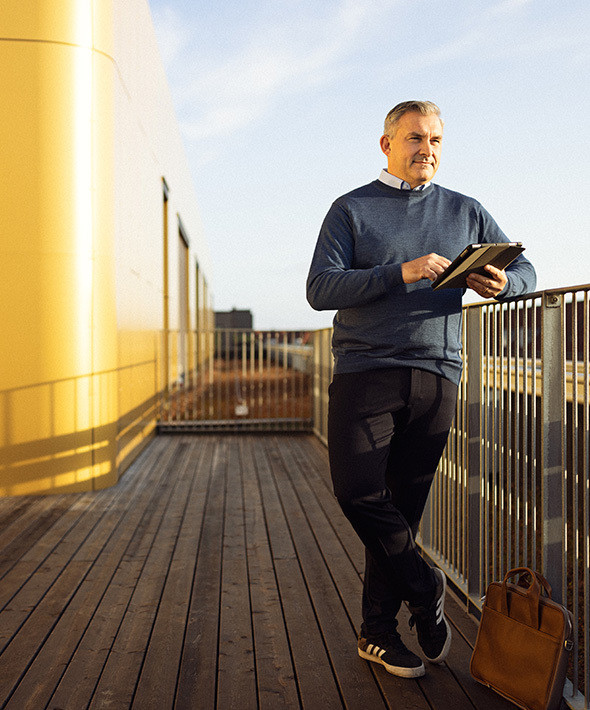 En mand står på en tagterrasse med en tablet og kigger ud over byen