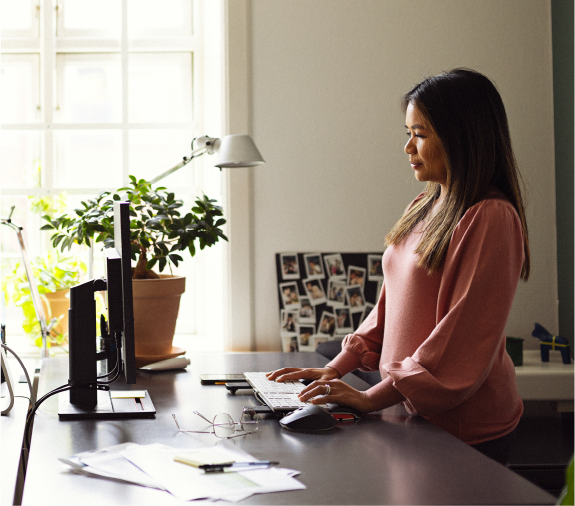 En kvinde står ved sit skrivebord og kigger ind i en computer